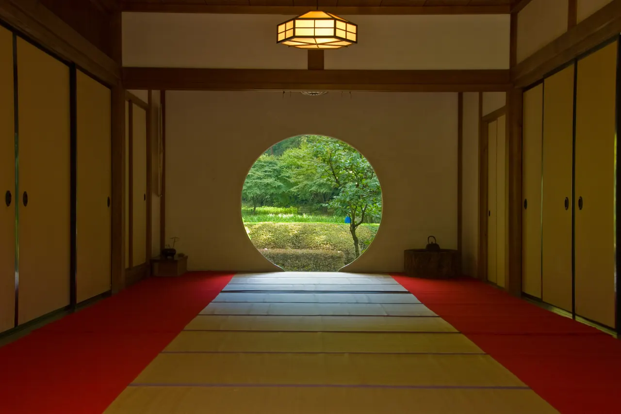 円い窓の向こうに、緑の庭が見える畳の間